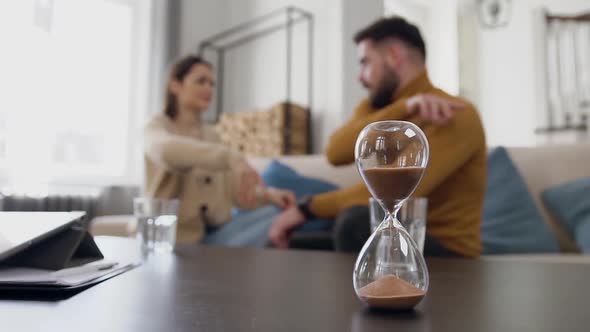 Sand Clock Counting Time while Young Raging Married Couple Quarreling alt
