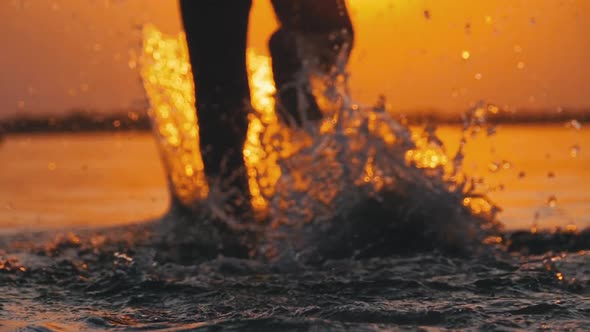 Silhouette of Legs of Boy Running Into the Water at Sunset and Creating Splashes. Slow Motion alt
