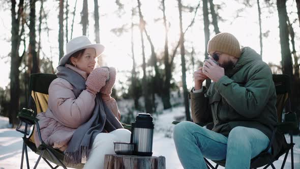 Couple Drinking Hot Tea in the Woods in Winter Enjoying Camp Life