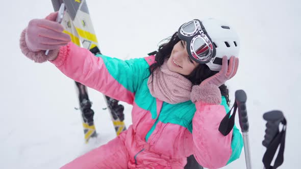 High Angle View of Charming Slim Woman Taking Selfie Sitting on White Snow at Winter Resort alt