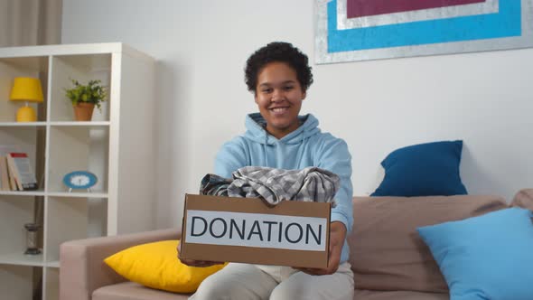 Smiling Afro-american Woman Holding Donation Box with Clothes Posing at Camera alt