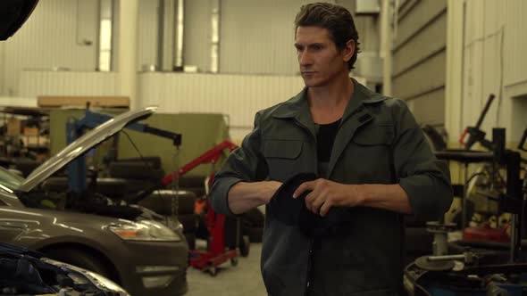 Video shot of the serious adult auto mechanic walking through the garage and wiping his hands alt
