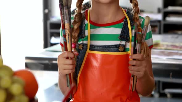 Portrait of cute schoolgirl standing with paintbrushes 4k alt