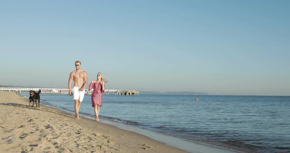 Fit couple walk down the beach with their playful dog alt