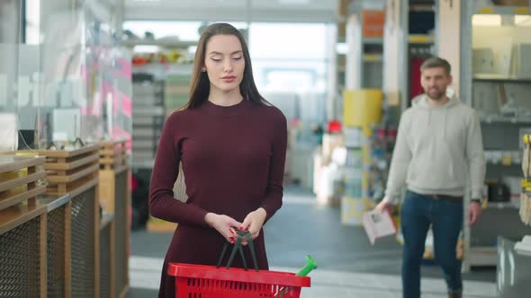 Middle Shot Portrait of Tired Young Caucasian Woman Waiting for Man Standing in Hardware Store alt
