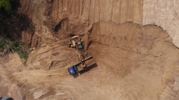 Aerial top view: yellow excavator pouring soil into tipper. alt
