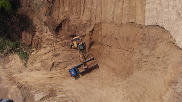 Aerial top view: yellow excavator pouring soil into tipper.