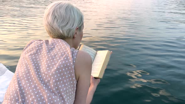 A Girl with White Hair Reads a Book on a Raft on a Lake alt