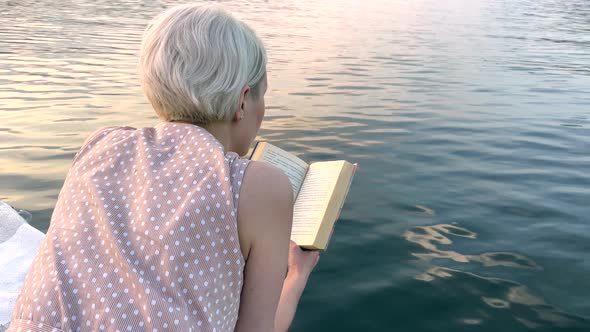 A Girl with White Hair Reads a Book on a Raft on a Lake
