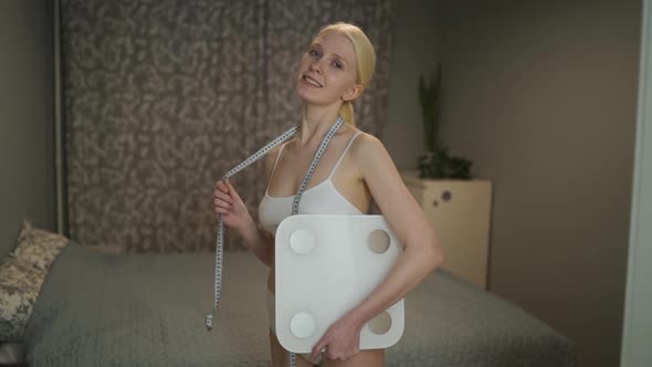 Young Slender Woman with a Measuring Tape Around Her Neck and Weights in Her Hands Posing alt