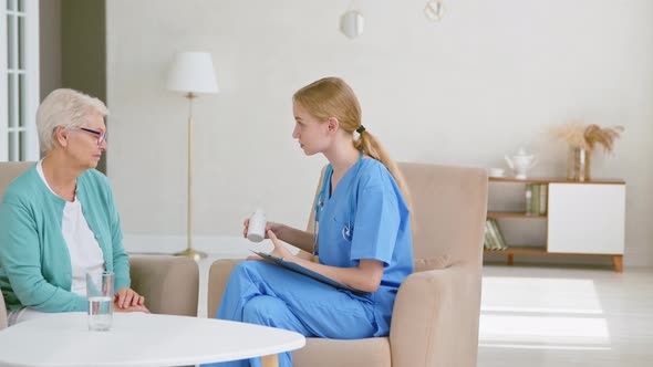 Skilled doctor with ponytail gives bottle of vitamins to senior patient woman alt