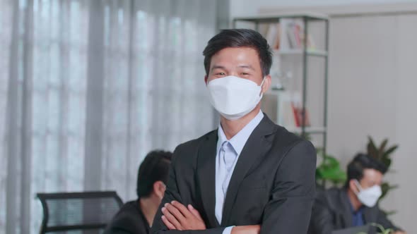 Portrait Of Young Asian Business Man Wearing Face Mask While Standing With Folded Arms At Office alt