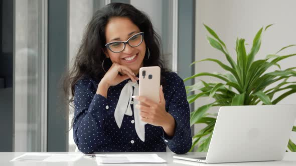 Happy mixed race businesswoman talking on smartphone by video chat at office.