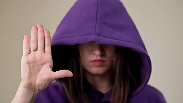 Woman Covering Her Face with a Hood Demonstrates a Gesture Indicating a Person's Need for Help alt