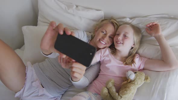 Ovear head view of Caucasian woman and her daughter taking selfie on bed alt