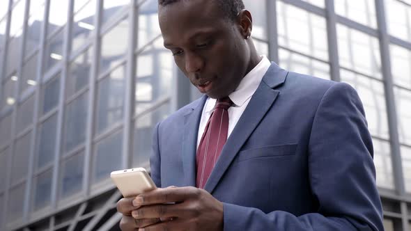 African  Businessman in The Street Types on His Smartphone alt