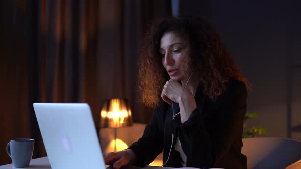 Attractive Curlyhaired Business Woman in a Business Suit Sitting Near a Laptop at a Work Table in alt
