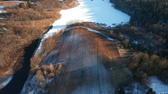 AERIAL: Rows of Plowed Earth Covered with Snow and Frost in Early Spring Near Frozen Lake