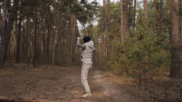 A Woman Make a Fun Dance in  Motion Next To a Pine Forest.