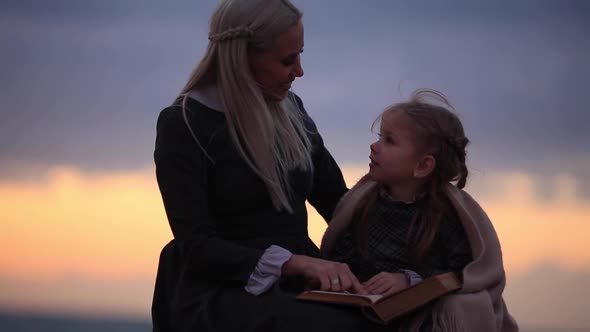 Woman with Girl Reading Book on Seashore