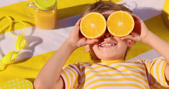 Happy child holding halves of orange fruit like a sunglasses. Slow motion