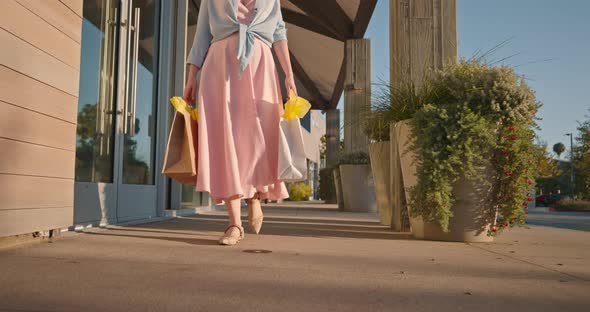 Woman in Pink Dress with Paper Bags Walking By Shopping Mall.  Slow Motion alt