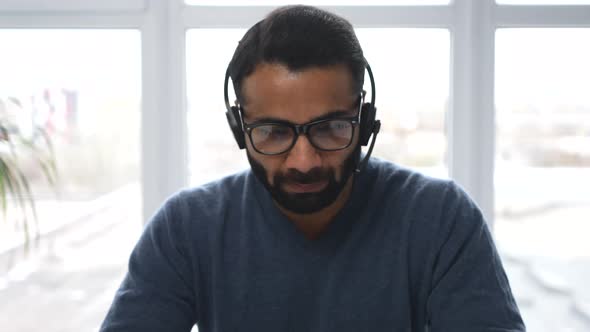 Front View of Midage Indian Male in Casual Wear Using Headset and Modern Laptop alt