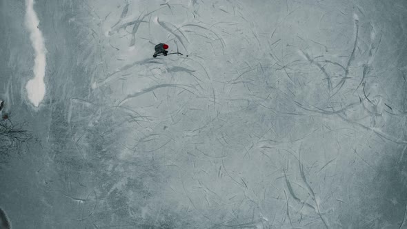 Drone looking down towards a single player playing ice hockey on a frozen pond or lake in Canada. alt