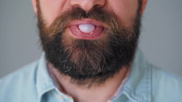 Close-up of a Bearded Man's Mouth Chewing Chewing Gum. Man Blowing Out a Bubble of Bubble Gum alt