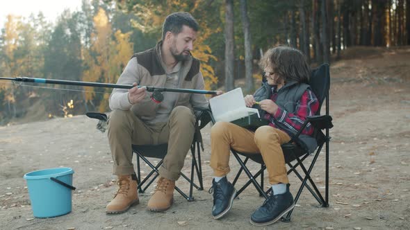 Caring Father Teaching Little Son to Catch Fish Discussing Bait and Rods on River Bank alt