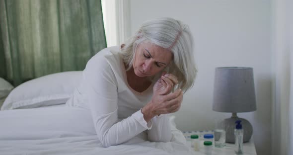 Sick or depressed senior caucasian woman sitting up in bed at home and holding her head alt
