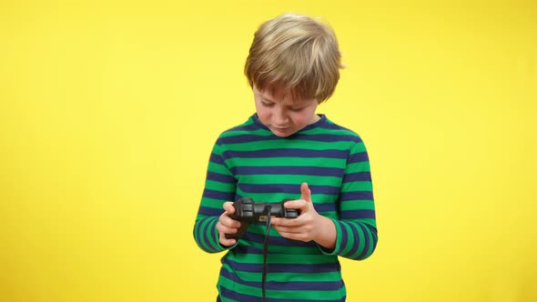 Portrait of Absorbed Blond Caucasian Boy Gaming on Game Console at Yellow Background alt