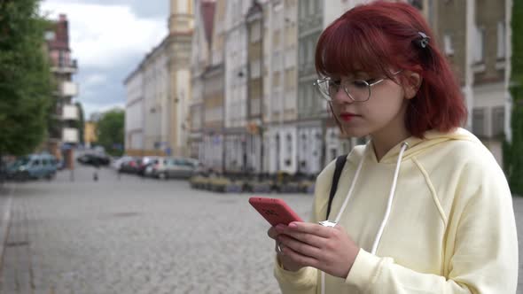 Young redhead Ukrainian teen girl with mobile phone on city street