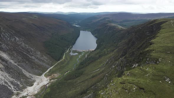 Overflying The Lush Green Forest And Mountain Range In Glendalough Overlooking The Upper Lake At Day alt