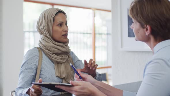 Smiling biracial woman talking and signing documents at reception at modern dental clinic alt