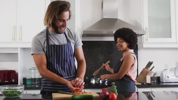 Mixed race couple wearing aprons cooking food together in the kitchen alt