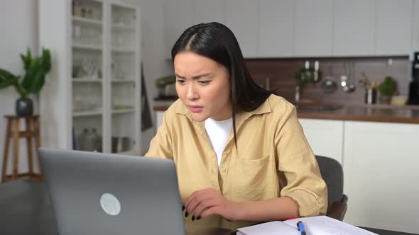 Sad Asian Woman Looking Annoyed and Stressed Sitting at the Desk Using a Laptop