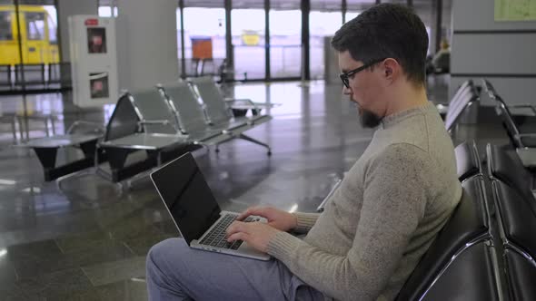 Guy Types on Laptop Sitting in Empty Waiting Room alt