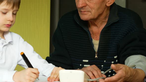 pensioner measures blood pressure at home, a 7-year-old grandson writes down the tonometer readings alt