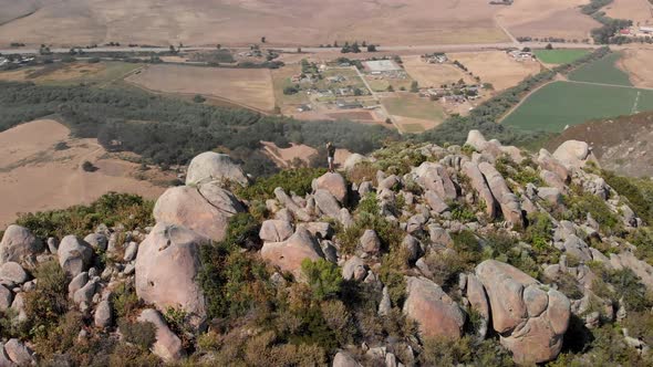 Drone flies around in complete circle while young man stands on mountain peak