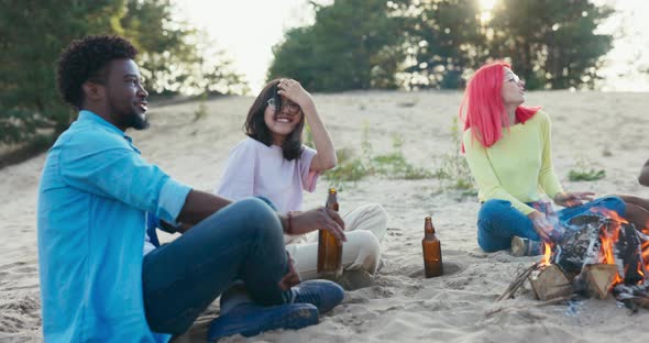 Friends Sitting on the Sand Near the Lake Spending Time Together Playing Relaxing By the Campfire alt