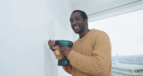 Young black man ready to drill hole into wall of new home alt