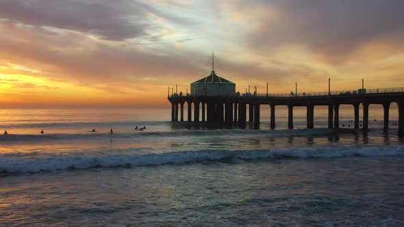 People Surfing Under the Manhattan Beach Pier at Sunset with a Lit Up Roundhouse Aquarium Roof in Ca alt