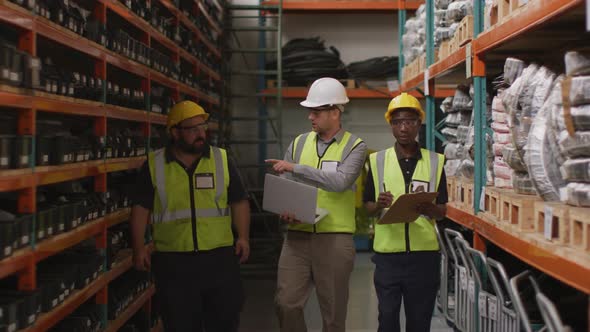 Two Caucasian and an African American male factory worker at a factory wearing hard hats and glasses alt
