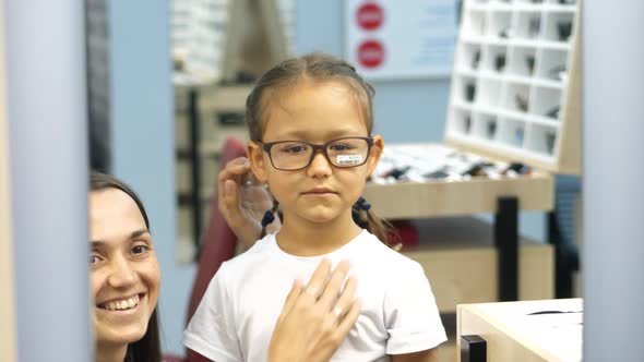Mother with Little Daughter Is Choosing Glasses at Optics Store