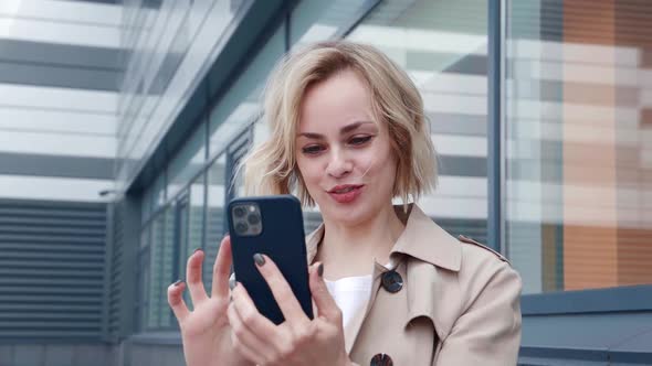 Portrait of Smiling Happy Young Woman in a Raincoat Using Smartphone Enjoying Surfing Social alt