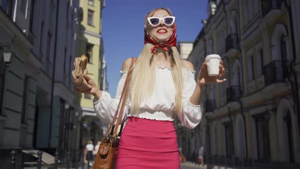 Beautiful Young Woman Walking on the Street Drinking Coffee and Eating Croissant. Attractive alt