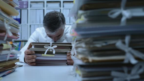 Overworked office worker hitting his head on paperwork