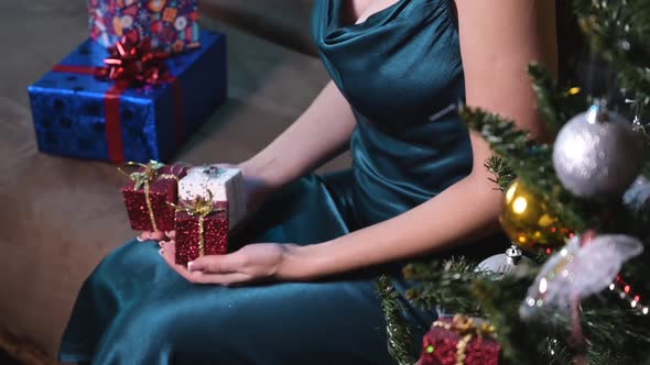 Young Woman in a Cozy Home Interior Holds Gift Boxes in Her Hands While Sitting Near the Christmas