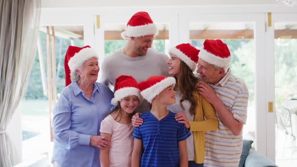 Portrait of family wearing santa hats smiling and standing together in the living room at home alt